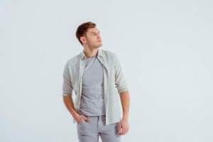 A guy wearing grey pants and a grey shirt is walking along.