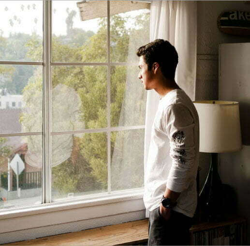 A young guy is standing while looking out a window.