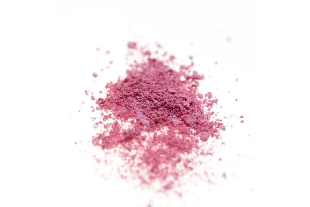 A small pile of loose, pink powder—resembling one of the more unusual types of cocaine—lies against a white background.