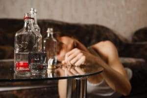 A man undergoing inpatient treatment lays on a table while holding a bottle of alcohol in a drug detox center.