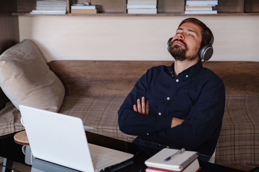 A man at a men's only rehab center, sitting at a desk with headphones and a laptop.