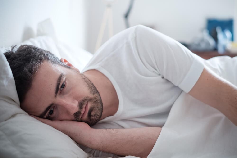 A man in an addiction recovery center, laying in bed with his head resting on his hand.