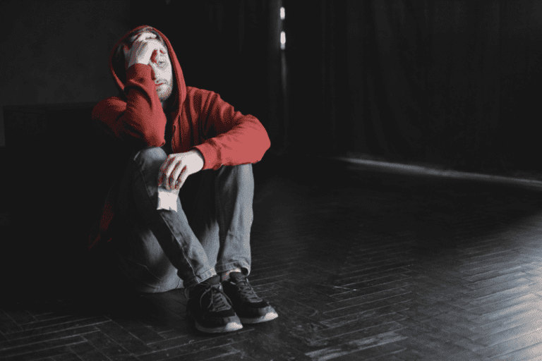 A depressed man on the floor in a dark room, suffering the mental effects of boofing drugs