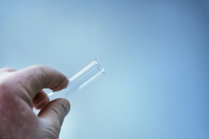 A person's hand holding a clear tube, illustrating an outpatient program for drug detoxification, on a blue background.